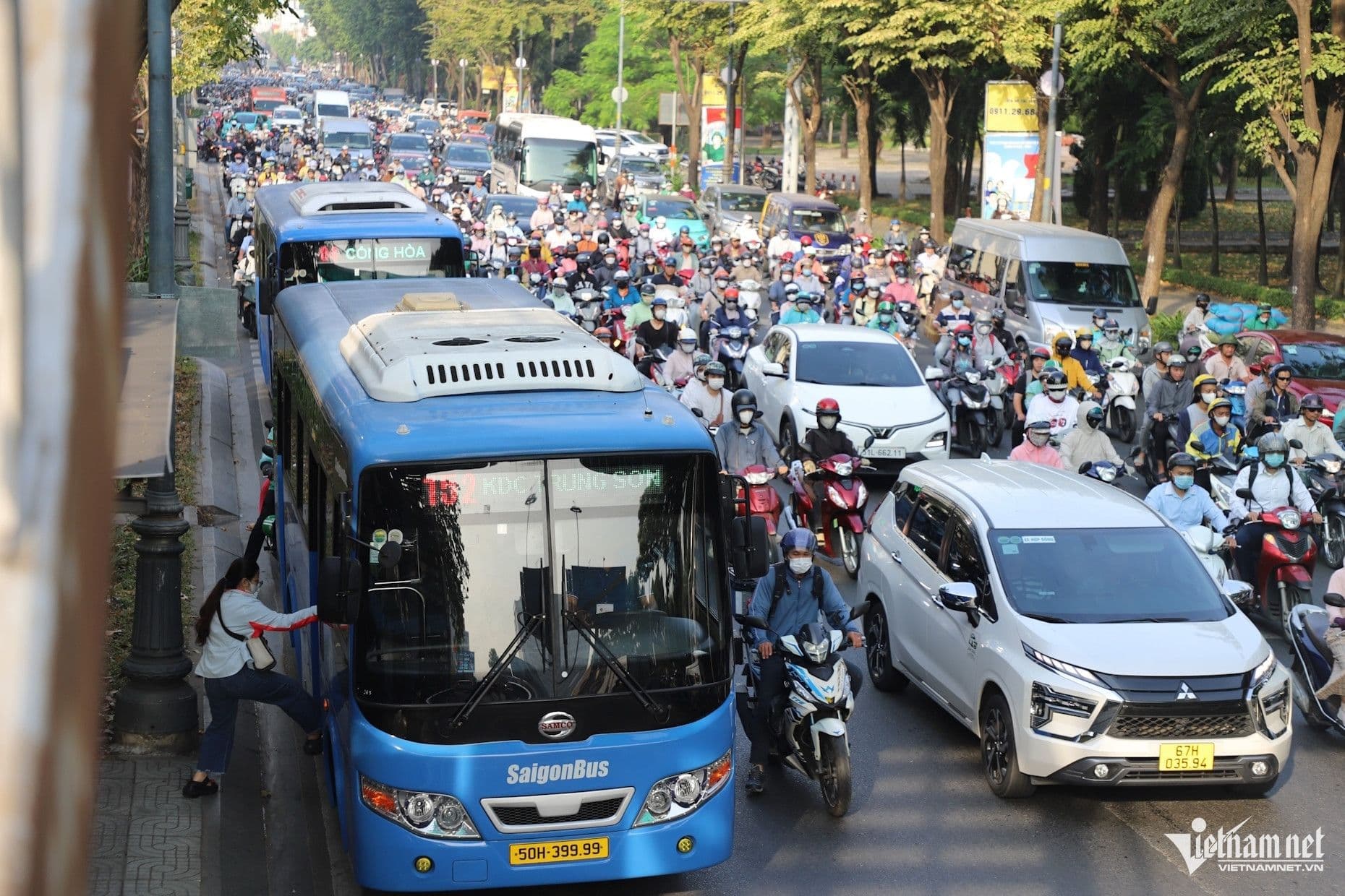 Xe buýt SaigonBus trên đường phố đông đúc tại TP.HCM giữa dòng xe máy và ô tô, thể hiện tình trạng ùn tắc giao thông và sự hiện diện của phương tiện công cộng.