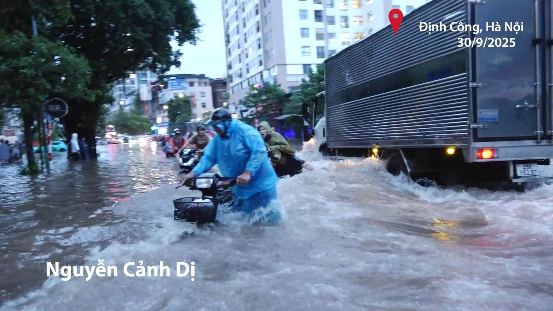 Xe máy chở người lớn và trẻ nhỏ chật vật di chuyển qua đoạn đường ngập sâu, bị sóng từ ô tô đánh ngã.